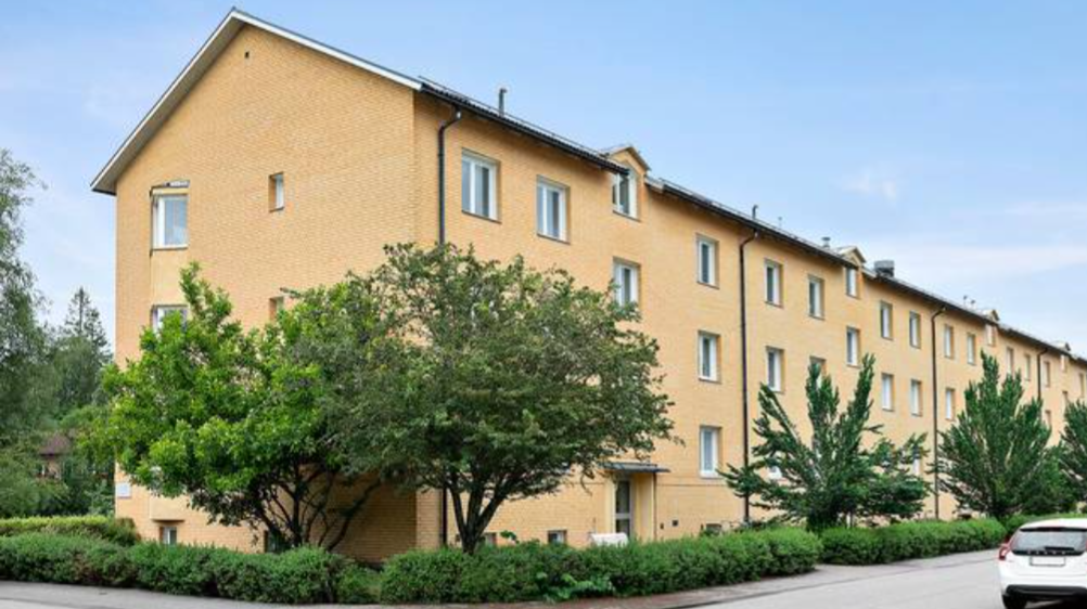 Ett gult trevåningshus med gröna träd runtomkring 