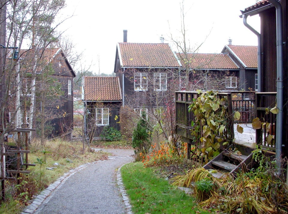 Hus i Understenshöjden byggda i trä med mörkbrun färg. Framför ena huset syns en lite rabatt med blommor. 
