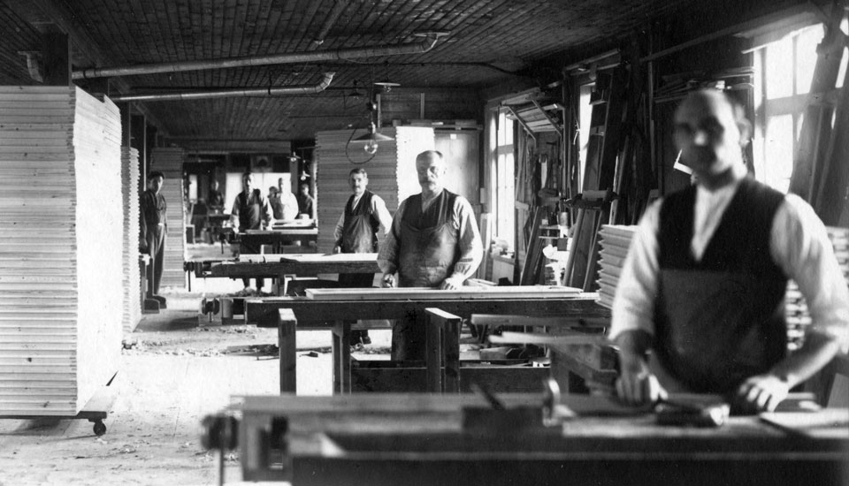 Män som står vid arbetsbänkar i HSBs snickerifabrik i Sparreholm.