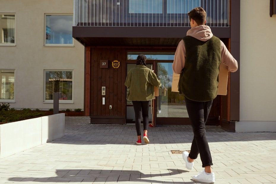Kille och tjej bär flyttkartonger in i bostadshus